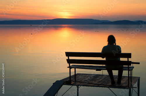 Sunset over lake Balaton with a sitting woman on an angler pier in the foreground