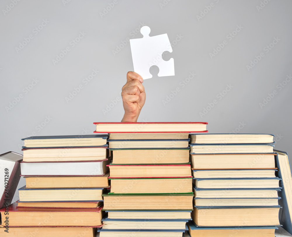 female hand holding a big white puzzle and a stack of books
