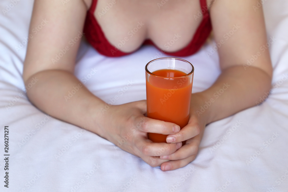 Woman drinks carrot juice, lying on the bed in the morning. Glass of fresh vegetable juice in female hands, concept of healthy diet, body care Woman drinks carrot juice, lying on the bed in the morning. Glass of fresh vegetable juice in female hands, concept of healthy diet, body care