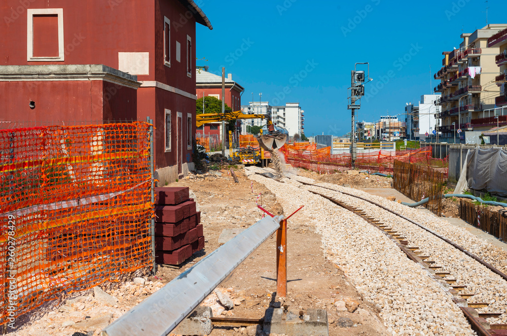 Fototapeta premium Close up bolted butt of rails and wooden sleepers laid on groundwork crushed stone. excavator bucket positions bowls for binary back-up