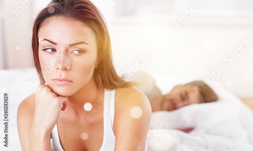 Photography Dissatisfied beautiful young woman in bed with sad expression on her face, sex problems in long relationship or marriage while man sleeping