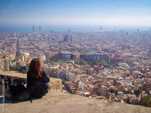 Lonely tourist girl sitting and watching the aerial skyline view of Barcelona (Spain) from the Bunker del Carmel in the sunny day