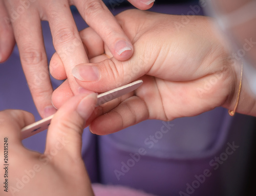 Woman receiving fingernail manicure service by professional  manicurist at nail salon. Beautician file nail manicure at nail and spa salon. Hand care and fingernail treatment at nail salon.