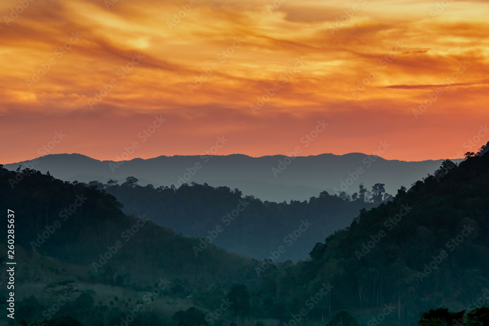 Beautiful nature landscape of mountain range with sunset sky and clouds. Mountain valley in Thailand. Scenery of mountain layer at dusk. Tropical forest. Natural background. Orange and golden sky.