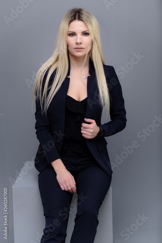 Portrait of happy smiling young cheerful businesswoman sitting. Success in business concept studio shot talking to a client. Gray suit.
