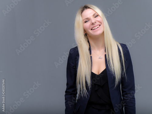 Portrait of happy smiling young cheerful businesswoman standing. Success in business concept studio shot talking to a client. Gray suit.