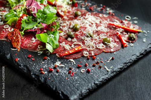 Beef carpaccio on black plate with mustard and parmesan.