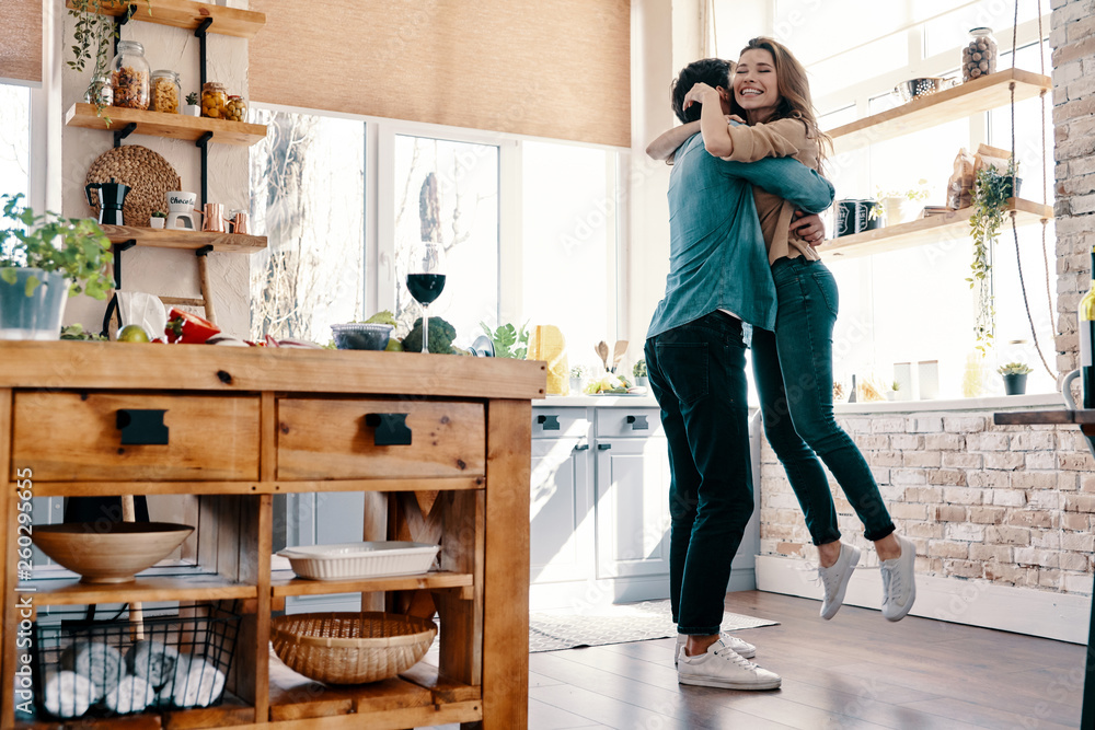 Totally in love. Full length of beautiful young couple in casual clothing dancing and smiling while standing in the kitchen at home - obrazy, fototapety, plakaty 