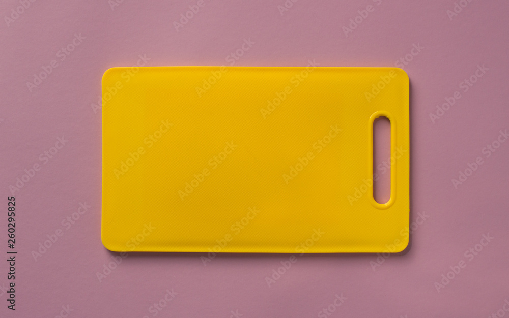 Colored yellow plastic cutting board on purple background, top view. Colored yellow plastic cutting board on purple background, top view.