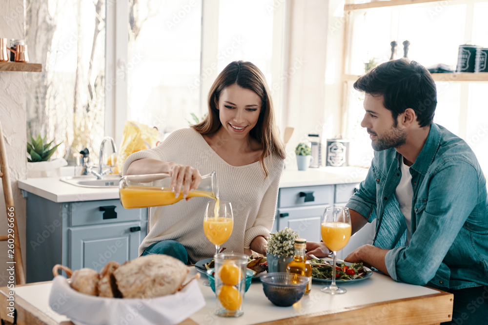 Enjoying time together. Beautiful young couple enjoying healthy breakfast while sitting in the kitchen at home Enjoying time together. Beautiful young couple enjoying healthy breakfast while sitting in the kitchen at home