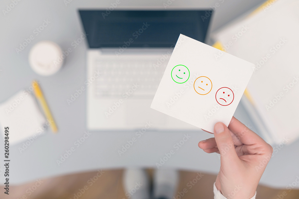 Woman clerk in the office holding paper sticker with set faces scale feedback. Customer satisfaction symbol. Woman clerk in the office holding paper sticker with set faces scale feedback. Customer satisfaction symbol.