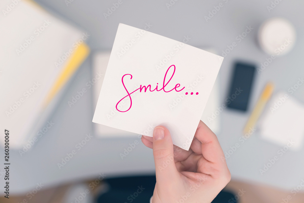 Woman clerk in the office holding paper sticker with the word: Smile. Motivation concept Woman clerk in the office holding paper sticker with the word: Smile. Motivation concept