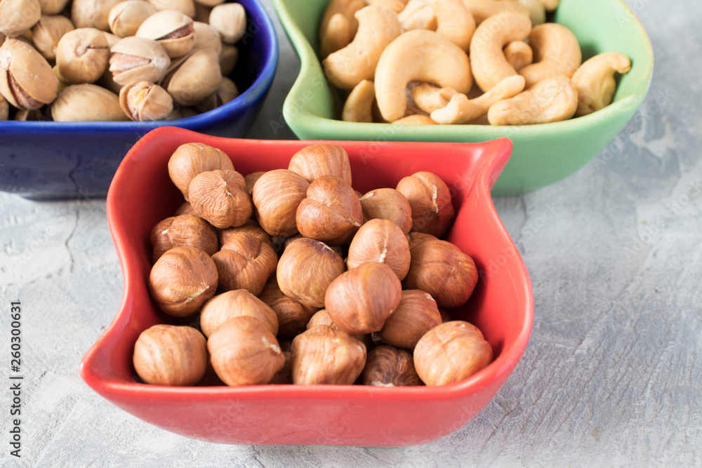 colorful bowls with mixed nuts on a gray background. Walnut, pistachios, almonds, hazelnuts and cashews, walnut. colorful bowls with mixed nuts on a gray background. Walnut, pistachios, almonds, hazelnuts and cashews, walnut.