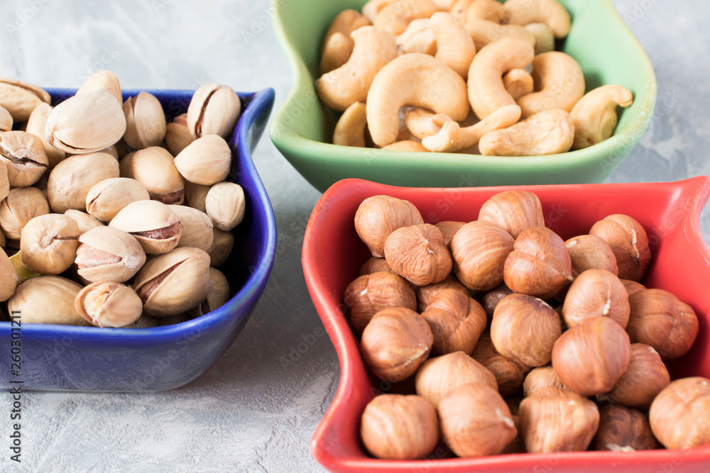 colorful bowls with mixed nuts on a gray background. Walnut, pistachios, almonds, hazelnuts and cashews, walnut. colorful bowls with mixed nuts on a gray background. Walnut, pistachios, almonds, hazelnuts and cashews, walnut.