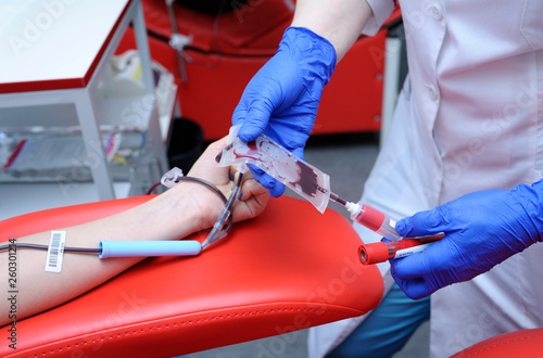 Nurse taking blood from the vain of a donor - hypodermic needle, tubes, container with blood