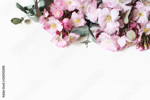 Fototapeta Naklejka Na Ścianę i Meble -  Closeup of decorative banner made of pink Japanese cherry blossoms and eucalyptus branches. Styled stock photo. Spring, Easter feminine floral composition. White background. Flat lay, top view.