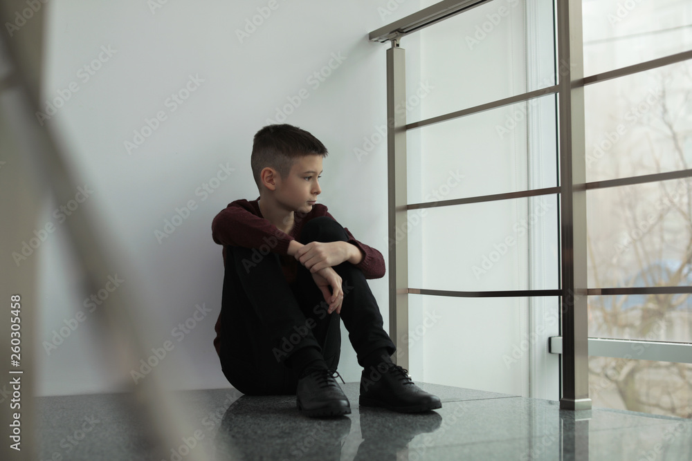 Upset preteen boy sitting on staircase indoors Upset preteen boy sitting on staircase indoors