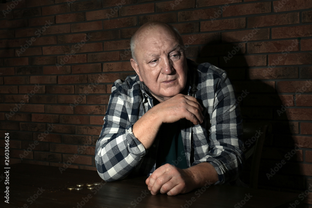 Poor senior man with coins at table near brick wall Poor senior man with coins at table near brick wall