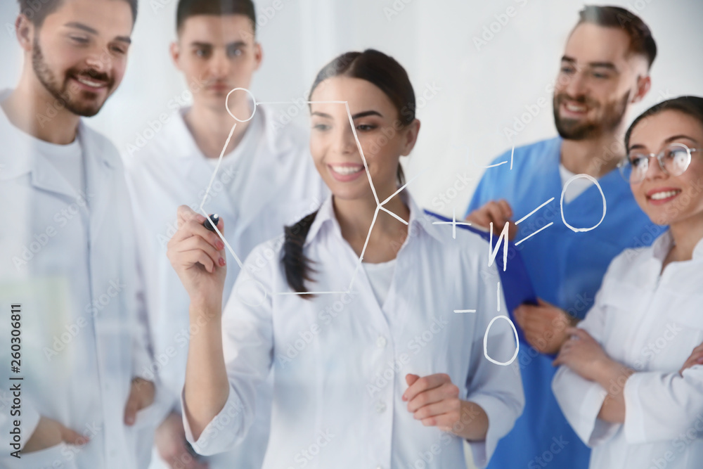 Medical students writing chemical formula on glass whiteboard in laboratory