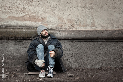 Slika na platnu Poor homeless man sitting near wall on street. Space for text