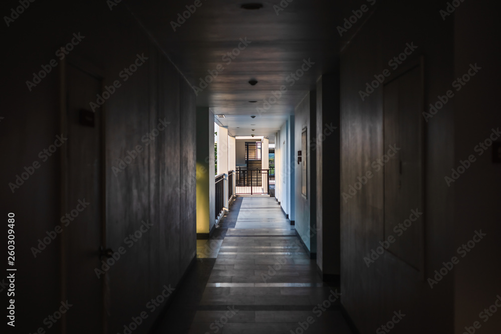 Perspective of empty corridor in apartment building with doors and and fire escape and light in the end of the way.