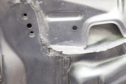 Close-up on the weld connecting the metallic parts of a car of silver color smeared with sealant and painted. Metalworking industry.