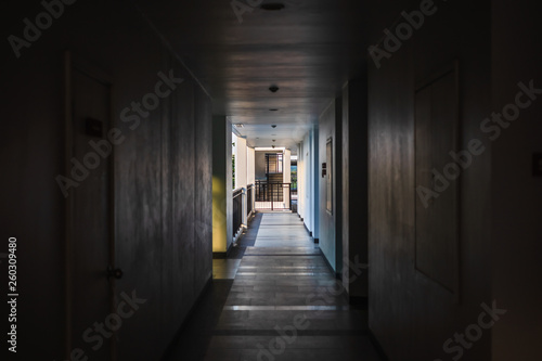Perspective of empty corridor in apartment building with doors and and fire escape and light in the end of the way.