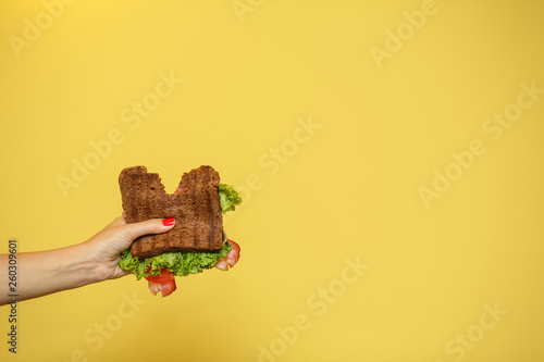 woman hands hold bitten sandwich on yellow background. Sandwich promotion concept