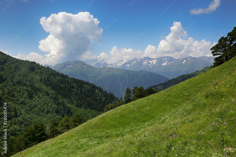 Beautiful nature in Russia, the Caucasus. Green hills in the valley, snow-capped mountains in the distance and clouds in the sky