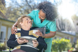 African female doctor playing and smiling with mature elderly woman on wheelchair in the garden using tablet