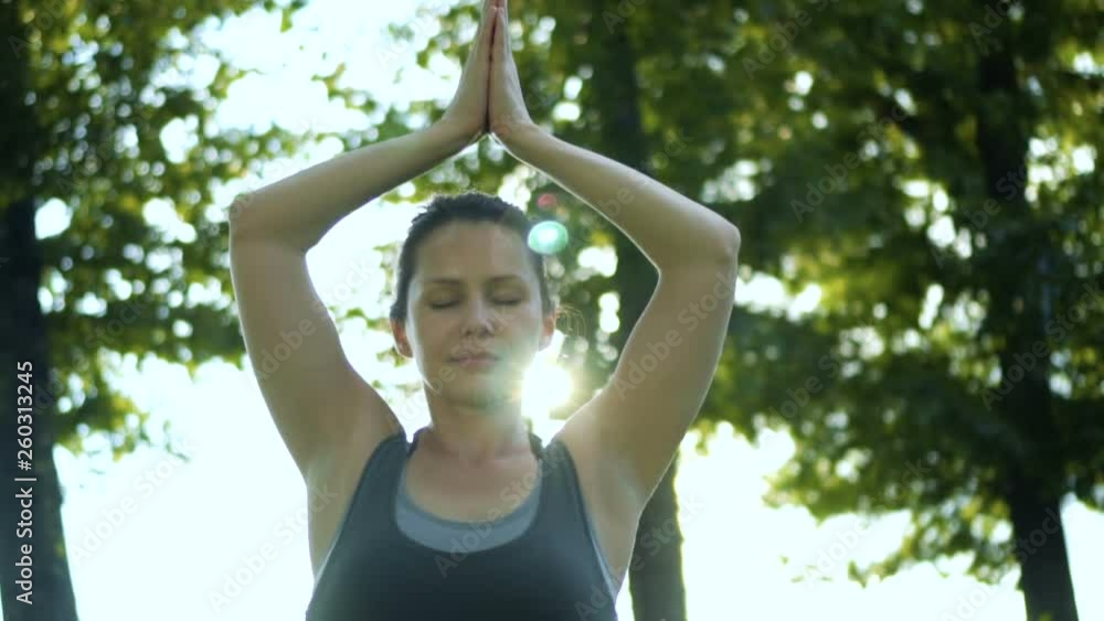 The Pretty woman holds her hands above head meditating while sitting in lotus pose. Yoga practicing in park. Rays of the sun The Pretty woman holds her hands above head meditating while sitting in lotus pose. Yoga practicing in park. Rays of the sun