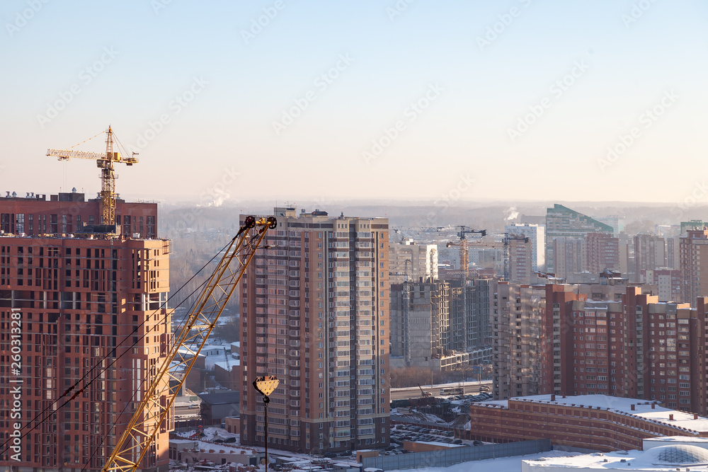 Aerial view of a new modern house under construction with a yellow tower crane, red lantern at the end of the crane, building materials on the top floor, bricks, cement, against a blue sky