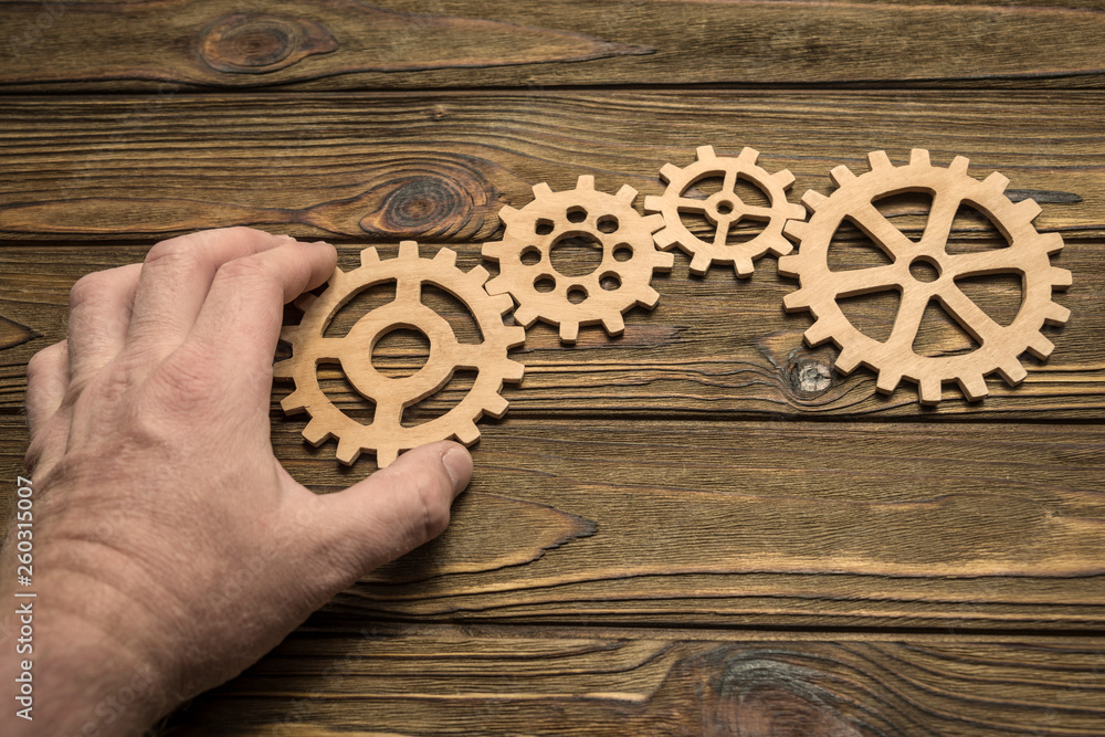 wooden gears, the hand of man on the background of wooden table. the mechanism of interaction. wooden gears, the hand of man on the background of wooden table. the mechanism of interaction.