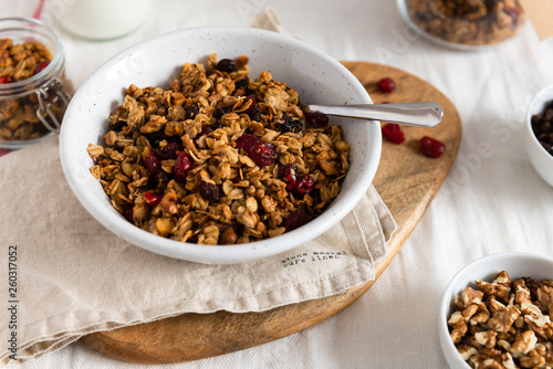 Bowl of homemade granola with nuts and fruits on white linen background. Side view