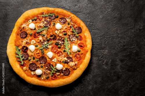 pizza with mozzarella, capers, arugula and tomatoes on black concrete background