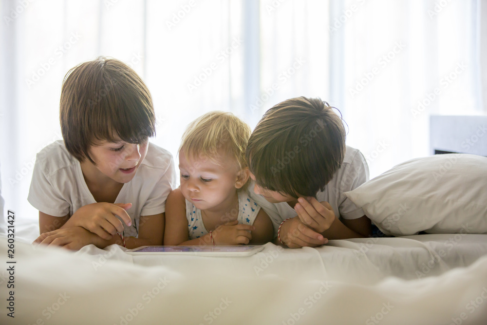 Brothers, playing in bed on tablet, enjoying summer holiday Brothers, playing in bed on tablet, enjoying summer holiday