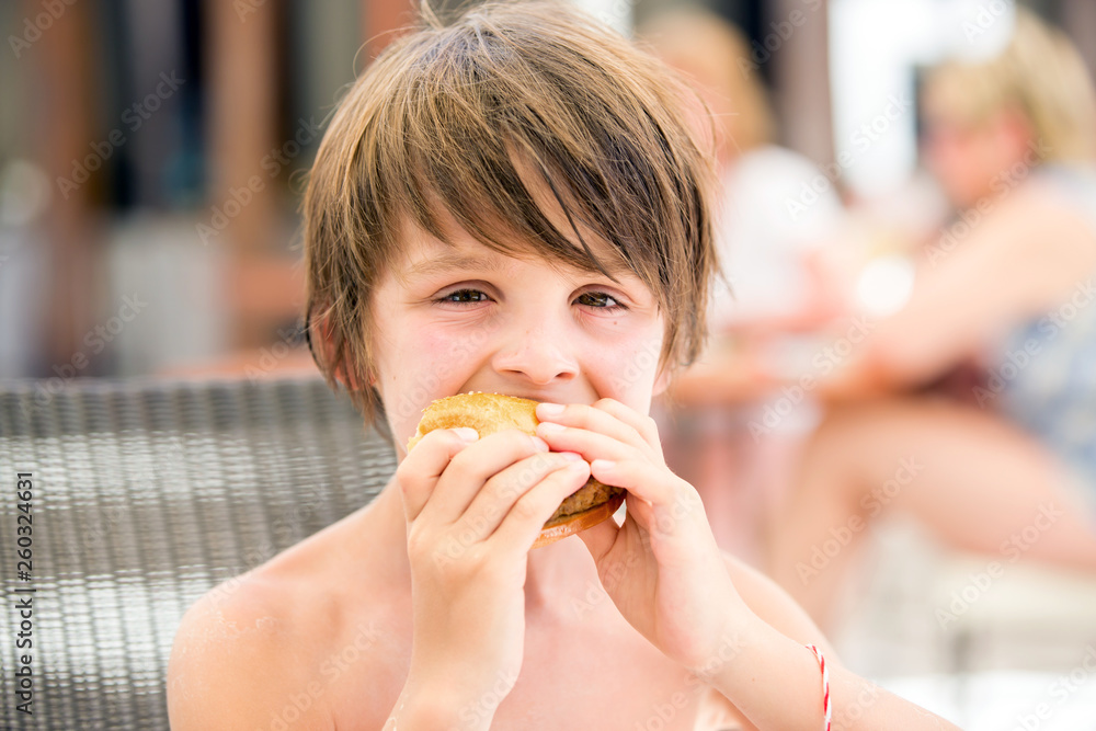 Sweet preschool boy, eating fresh hamburger in a restaurant on beach summer resort Sweet preschool boy, eating fresh hamburger in a restaurant on beach summer resort