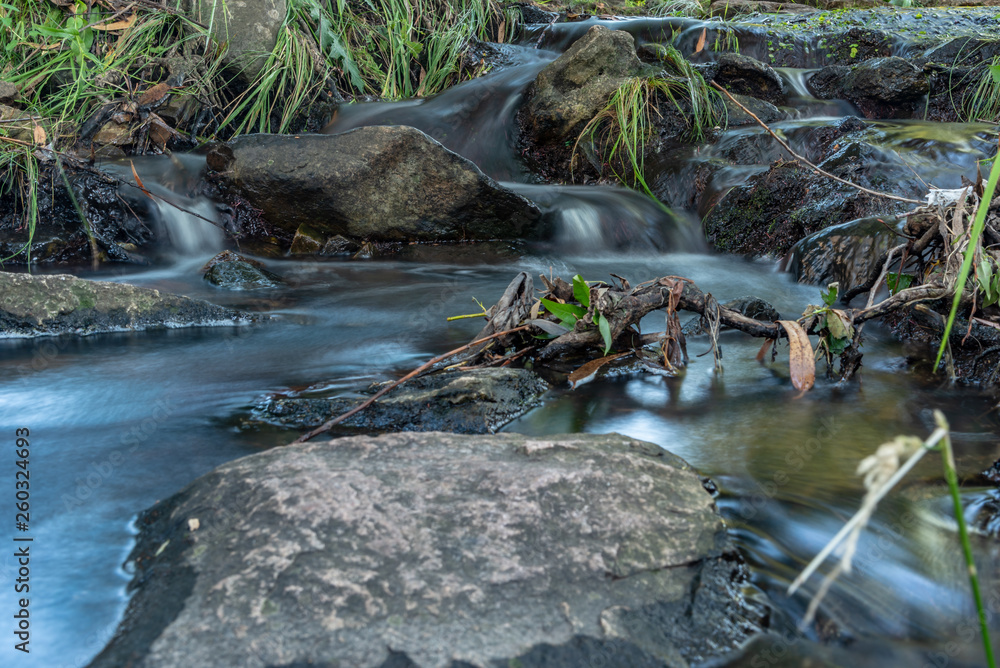 Small waterfall or cascade captured near the water surface full of rocks and plants with long exposure Small waterfall or cascade captured near the water surface full of rocks and plants with long exposure