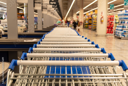 A lot of supermarket carts handles with shallow depth of field with a part of the market view blurred