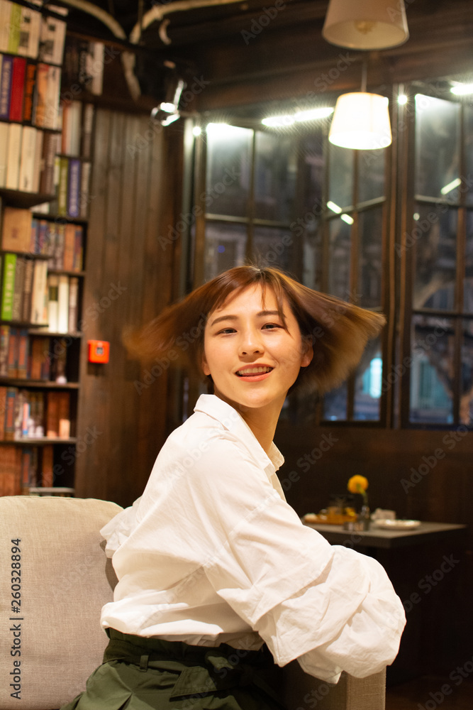 Asian chinese girl having a good time at a coffee shop in hangzhou, China. wearing a white shirt, smiling