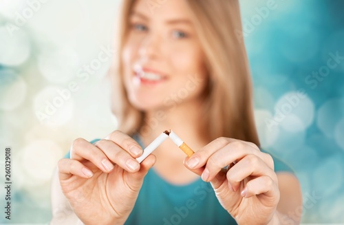 Young woman breaking cigarette on background