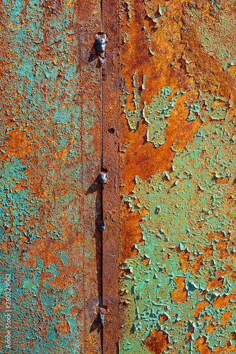 Texture of rusty metal, painted blue and green which becames orange from rust. Vertical texture of cracked paint on rusty welded steel sheets