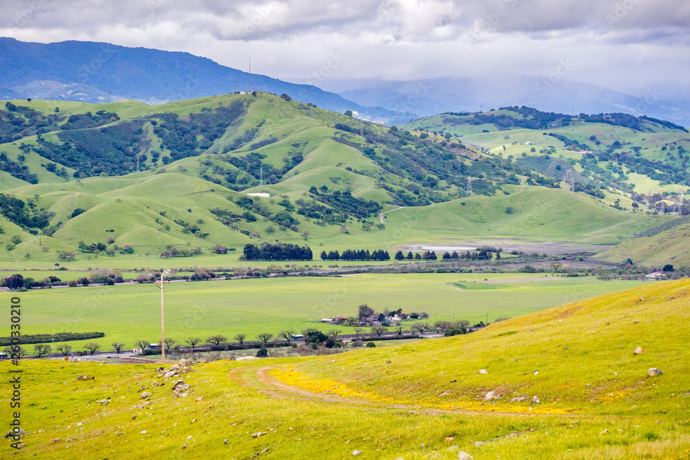 Verdant hills and valley in south San Francisco bay area on a rainy spring day; hiking trail visible in the foreground; San Jose, California