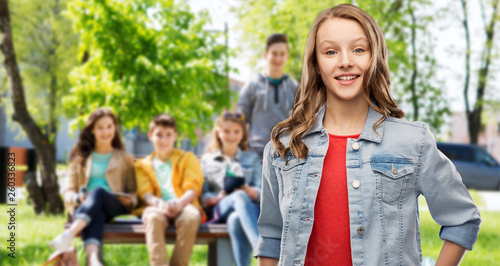 teen and people concept - smiling teenage girl with long hair in denim jacket over her friends on summer background