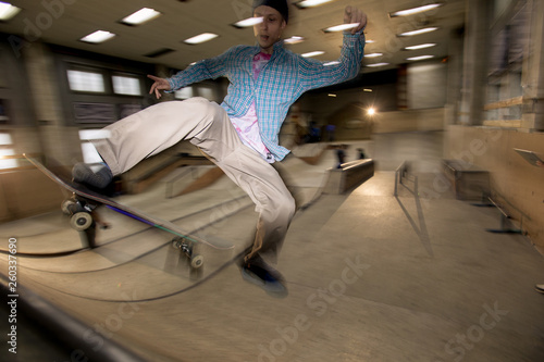 Action shot of contemporary young man doing skating stunt on ramp at skateboard park, shot with flash
