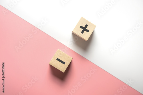 The concept of opposites, wood blog with plus and minus  on white and pink background, flat lay, copy space, top view. photo
