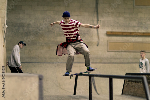 Action shot of contemporary young man sliding on rail at skateboard park, copy space