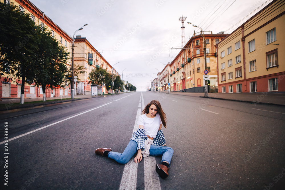 Girl in a plaid shirt and jeans. Girl posing sitting on the middle of the road.