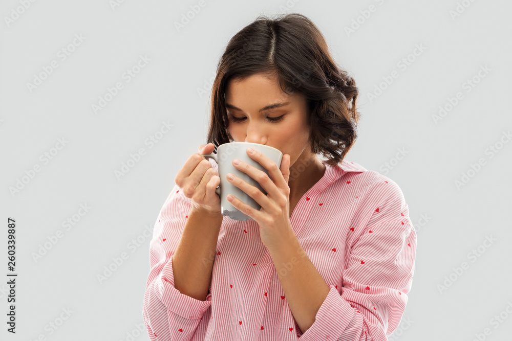 people and bedtime concept - happy young woman in pajama drinking coffee from mug over grey background people and bedtime concept - happy young woman in pajama drinking coffee from mug over grey background