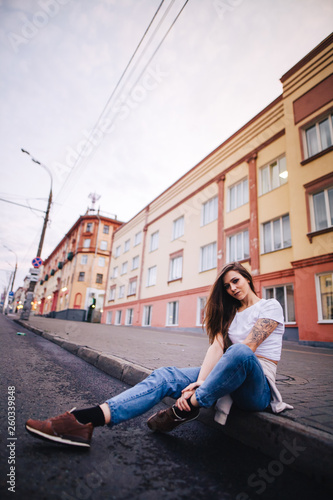 The girl sits on the edge of the roadway. Street urban style.